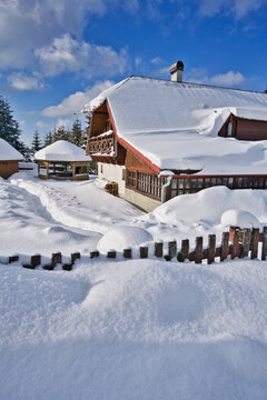 View of a snow-covered chalet glows warmly under a blue sky, contrasting with the pristine white landscape, Donovaly, Banskobystricky kraj, Slovakia.