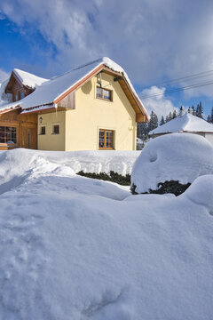 View of a cozy yellow house nestled in a deep blanket of pristine white snow under a bright blue sky in Polianka, Donovaly, Banskobystricky kraj, Slovakia.