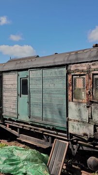 Dilapidated wooden railway carriages stand forgotten in a quiet shunting yard, their warped panels cracked and splintering with age.  Panning shot.
