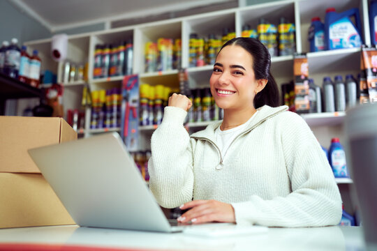 Happy Latina Small Business Owner Celebrating Online Sale Using Laptop in Auto Parts Store