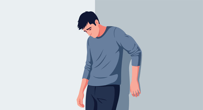 A sad young man leaning against a grey wall feeling lonely and depressed