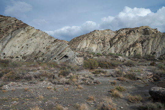 The arid landscape of Tabernas Desert in Almeria, Spain, with rugged hills, sparse vegetation, and rocky outcrops under a cloudy sky. It&rsquo;s a popular filming location