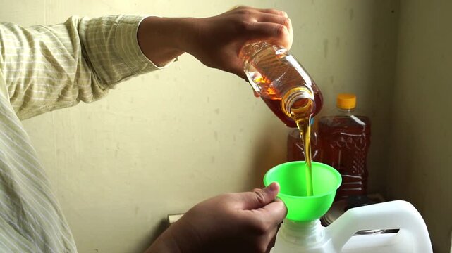 Close up of woman hands pouring used cooking oil through funnel into plastic jerrycan, household waste collection and recycling concept