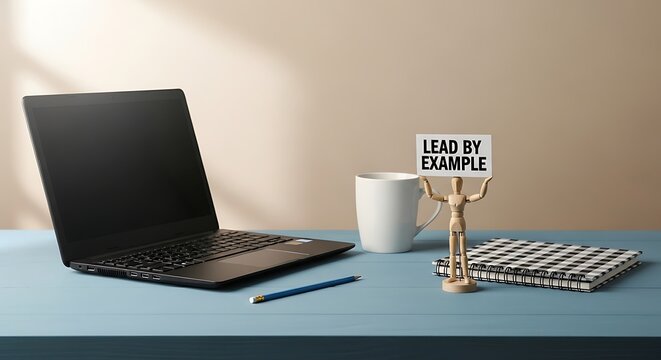 Minimalist workspace with laptop, coffee, and lead by example sign on light desk