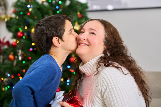 Son, christmas day gift and kiss on sofa in living room of home for love, celebration or surprise.