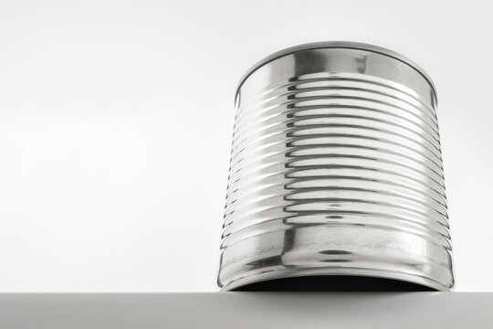 A shiny tin can standing on the edge of a white surface on a light background, in a minimalist style copy space Canned food and food stocks concept