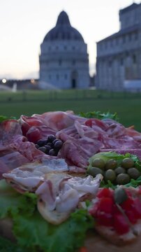 Delicious Italian appetizers served on a wooden board with a scenic view of the Leaning Tower of Pisa