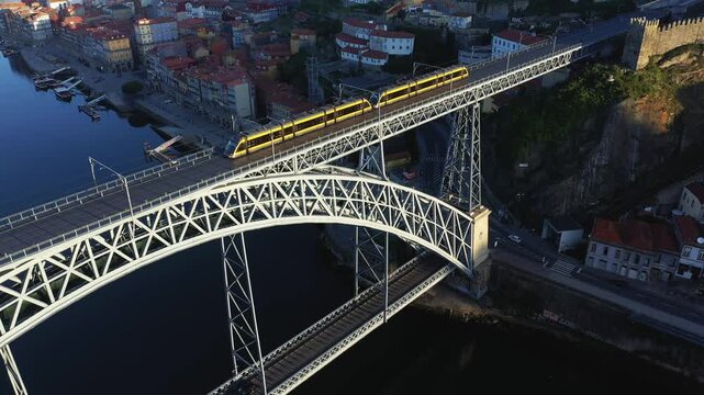 Drone shot of the Dom Luis I Bridge with a yellow tram crossing over the Douro River in Porto, Portugal, with cityscape in the background.