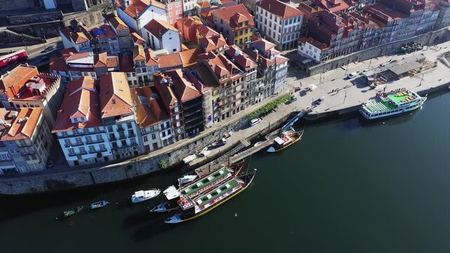 High angle view of colorful historic buildings and boats along the Douro River waterfront in central Porto, Portugal. Bright rooftops and calm water create a vibrant cityscape.