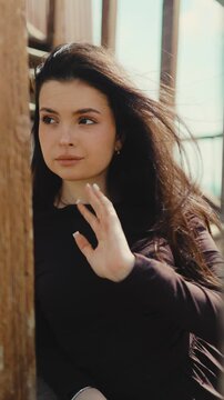 A close-up portrait of a young woman looking away as wind blows through her dark hair in bright sunlight. Beauty, skin, natural, look, freedom, dream, youth, lifestyle, wind, morning, soft