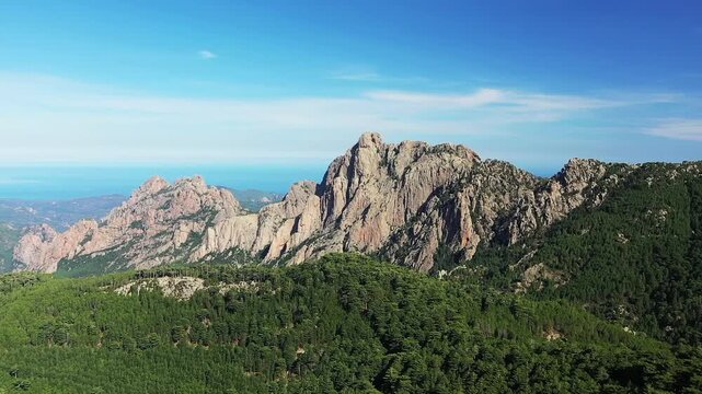 Scenic view of the rugged Col de Bavella mountains surrounded by dense green forest under a clear blue sky in Corsica, France.