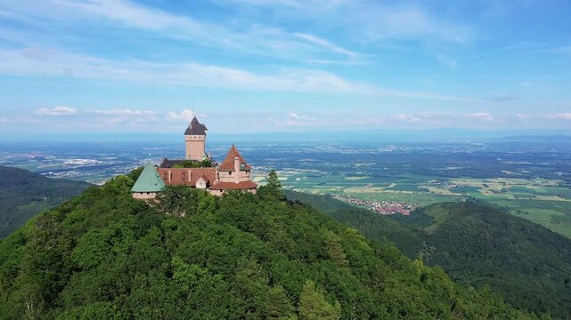 Aerial view of Chateau du Haut Koenigsbourg perched atop a forested hill, overlooking the Alsace plain in France on a clear summer day.