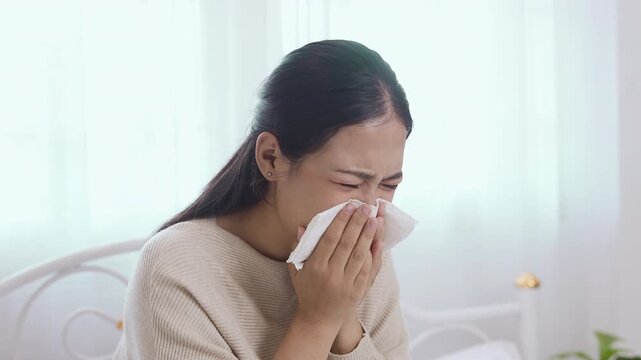 women sneezing into tissue while sitting on bed, cold and flu symptoms, allergy reaction, sick at home, healthcare concept, illness recovery, hygiene and protection.