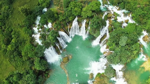 Stunning aerial shot of Ban Gioc Waterfall cascading through lush green forest and turquoise river in northern Vietnam.