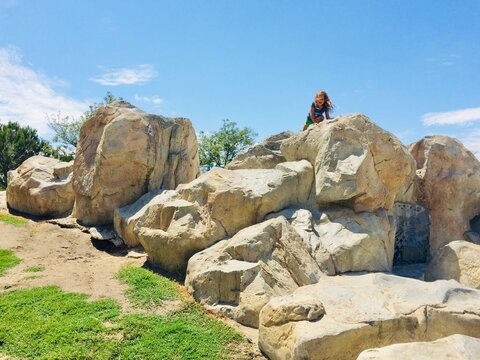 Young Girl in shorts climbing On play Boulders in a playground With Her Arms outstretched, Emerald Glen Park, Dublin, California, USA