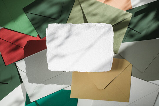Full frame overhead view of a piece of deckle edge card on assorted multi coloured envelopes on a table in dappled light