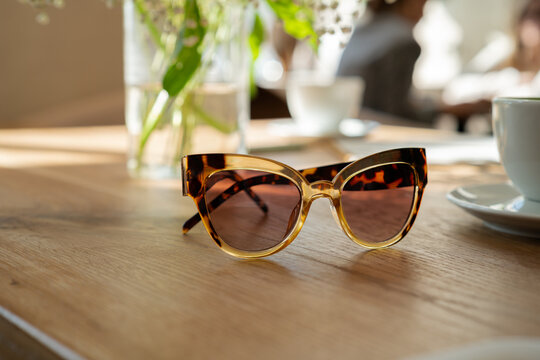 Close-up of a pair of Stylish tortoiseshell sunglasses on wooden table in  cafe
