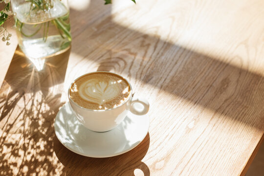 Close-up of a cup of coffee and floral shadows on a wooden table on a sunny morning