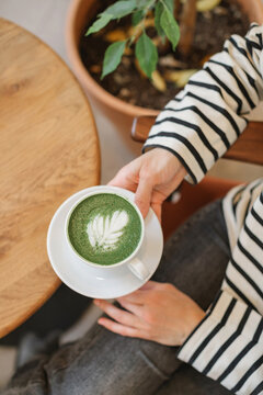 Overhead view of a woman sitting in a caf&eacute; drinking a hot matcha latte