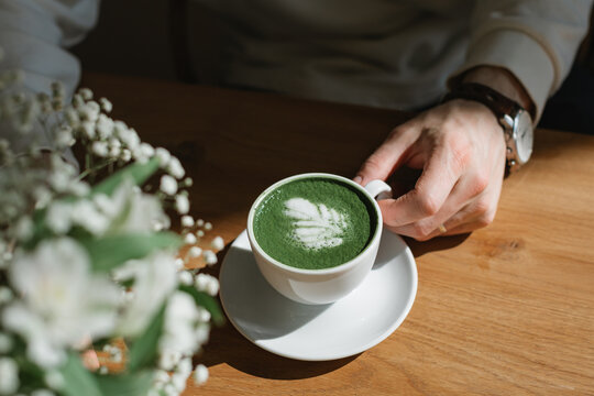 Close-up front view of a man sitting at a table drinking a hot matcha latte