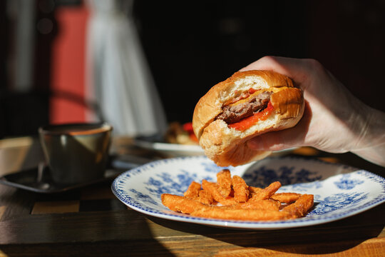 Close-up of a man sitting in a cafe on a sunny day eating a hamburger with sweet potato fries