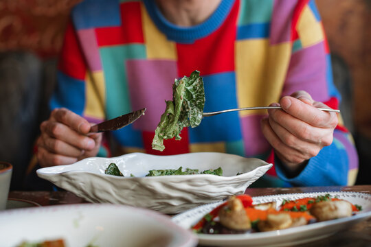 Close-up of a man sitting at a table eating a green salad with smoked stracciatella cheese and assorted roasted vegetables