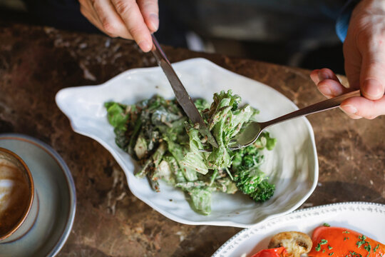 Overhead view of a man sitting at a table eating a green salad with smoked stracciatella cheese and a coffee