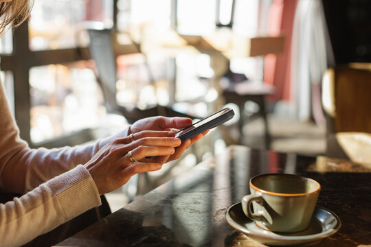 Close-up side view of a woman sitting in a cafe on a sunny day using her mobile phone during a coffee break
