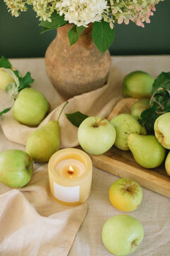 Close-up of a Bunch of fresh hydrangeas in a rustic clay jug on a table with a scented candle and apples on a wooden chopping board