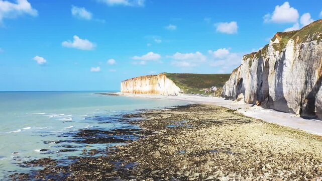 Scenic view of white chalk cliffs and rocky shoreline under a bright blue sky at Les Petites Dalles, Normandy, France. Tranquil seascape with natural coastal beauty.