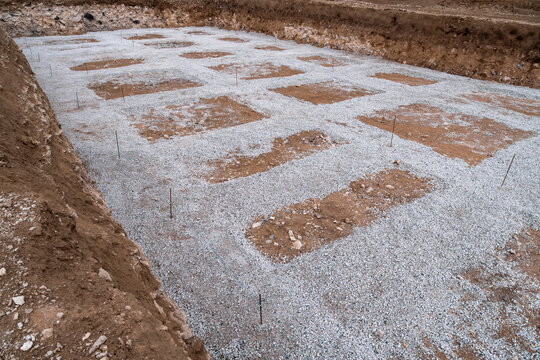 Foundation trench with gravel bedding and marked footing positions at construction site, soft focus texture.