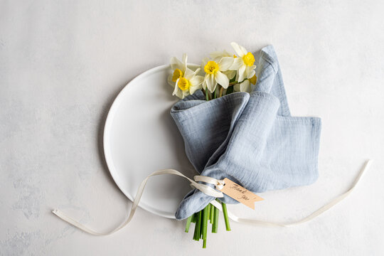 Overhead view of a bunch of daffodils tied with a ribbon and gift tag with the words thank you on a ceramic plate