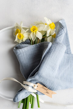 Overhead view of a bunch of daffodils tied with a ribbon and gift tag with the words thank you on a ceramic plate
