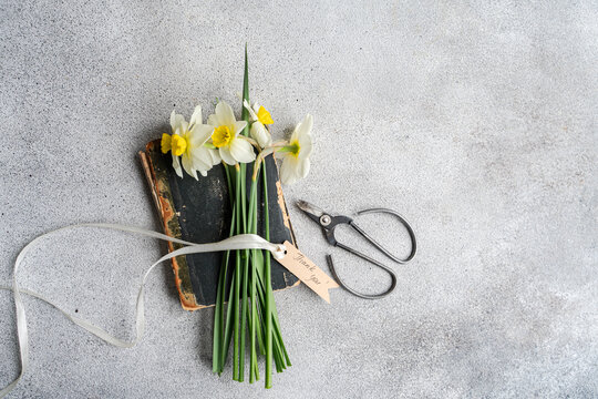 Overhead view of a bunch of daffodils tied with a ribbon and a gift tag with the words thank you on top of an old book next to a pair of scissors