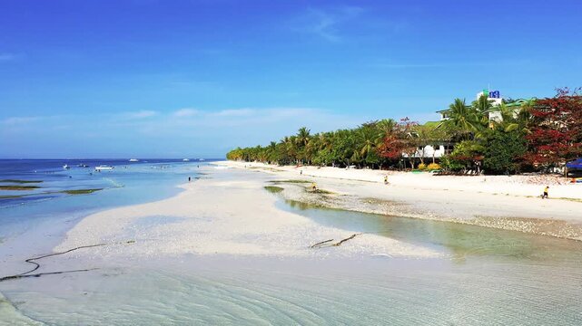 Wide sandy beach lined with palm trees and clear blue sky on Panglao Island, Philippines. Tranquil tropical coastline with people enjoying the seaside.