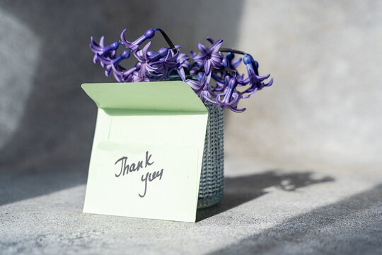 Thank you note in front of a vase of blue hyacinths on a table in sunlight