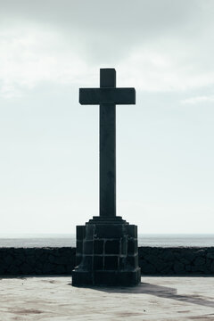 Solitary stone cross monument by the sea under grey sky