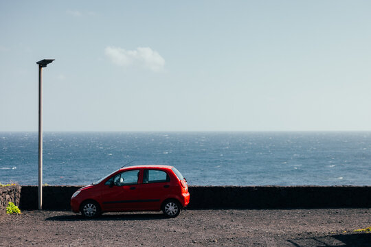Red compact car parked by Atlantic Ocean on La Palma