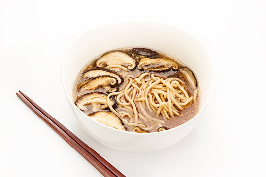 Bowl of Asian noodle soup with shiitake mushrooms and chopsticks on a white background