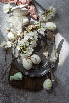 Overhead view of a rustic spring place setting with cherry blossoms on a pewter plate, assorted Easter decorations and a glass of water on a table