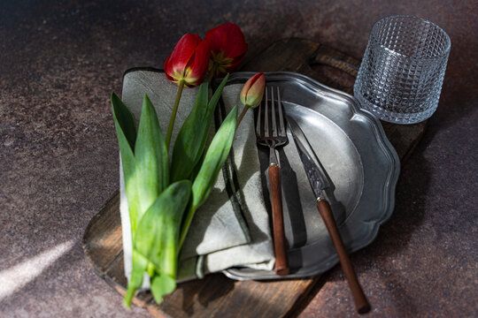 Overhead view of red tulips on a rustic place setting with a pewter plate on a table