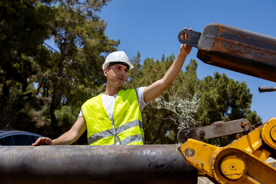 Construction worker inspecting excavator arm at worksite