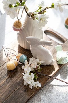 Close-up of a Spring table setting with a vase of cherry blossoms with assorted Easter ornaments on a wooden chopping board
