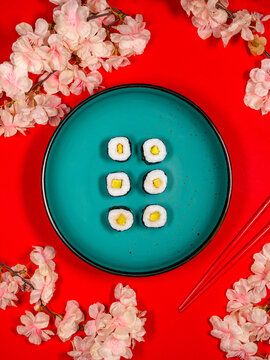 Maki-Sushi mit Avocado auf einem t&uuml;rkisfarbenen Teller vor rotem Hintergrund