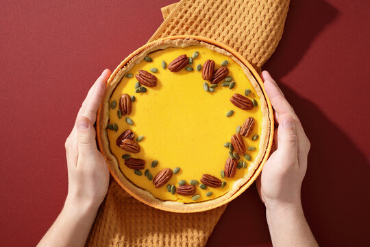 Hands holding pumpkin pie with pecan and seed topping