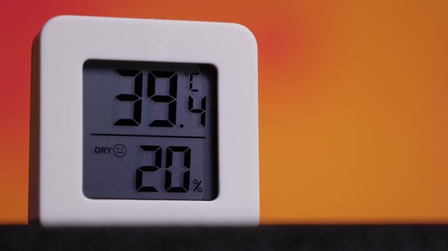 Square-shaped white digital thermometer and hygrometer device shows a temperature reading of 39.6 degrees Celsius and a humidity level of 20%, indicated as dry with a neutral face icon.