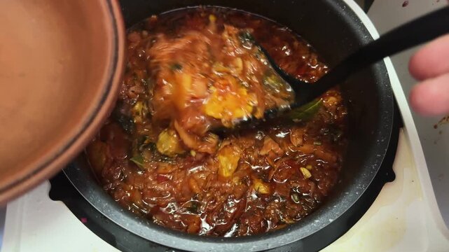 Pouring red borscht to clay bowl from multi-cooker pot