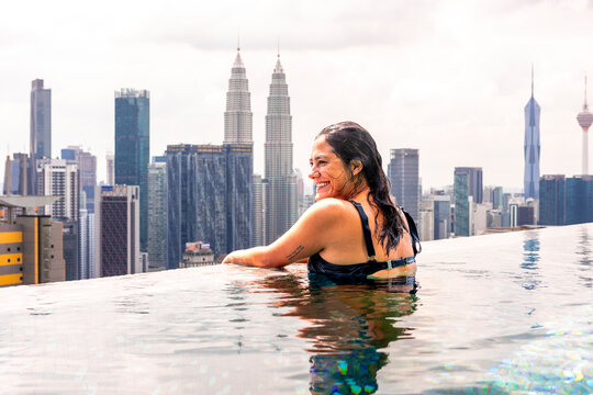Woman relaxing in rooftop pool with Petronas Towers view