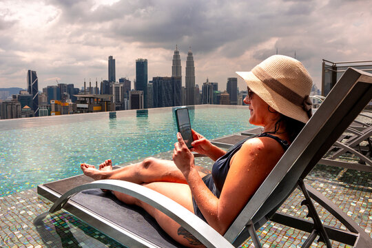 Woman relaxing by rooftop pool with Petronas Towers view