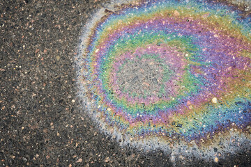 Obraz premium Iridescent oil slick creating colorful rainbow pattern on dark asphalt, symbolizing fuel pollution and liquid waste